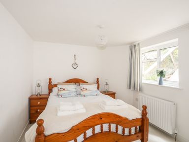 A bedroom with a wooden bed and two bedside tables with lanterns by a window with curtains and a vase with flowers at Isfryn in Llanengan near Abersoch