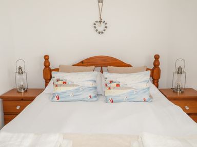 A bed with wooden headboard two painted pillows two beige pillows bedside tables with glass lanterns and a heart decoration on the wall at Isfryn in Llanengan near Abersoch