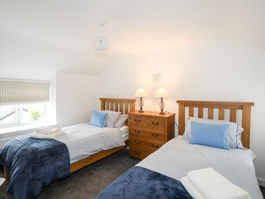 A bedroom with two single wooden beds striped bedding blue cushions a wooden chest of drawers and two lamps at Isfryn Llanengan near Abersoch