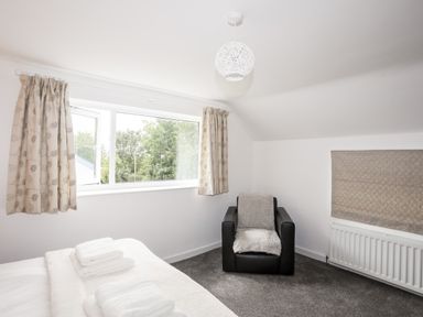 A bedroom with a bed, towels, armchair, window with curtains and radiator at Isfryn in Llanengan near Abersoch