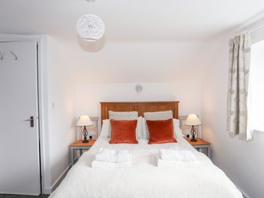 A bedroom with a double bed two bedside tables with lamps two orange cushions and folded towels at Isfryn in Llanengan near Abersoch