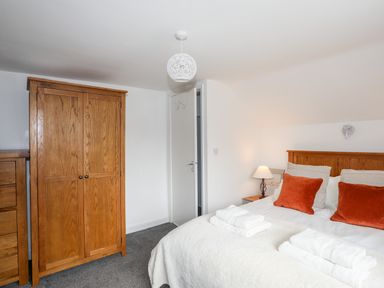 A bedroom with a wooden wardrobe a bed with orange pillows and white towels on top at Isfryn in Llanengan near Abersoch