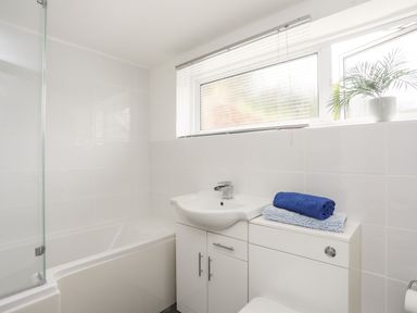 A bathroom with a bathtub sink cabinet towels and a potted plant on the window ledge at Isfryn in Llanengan near Abersoch