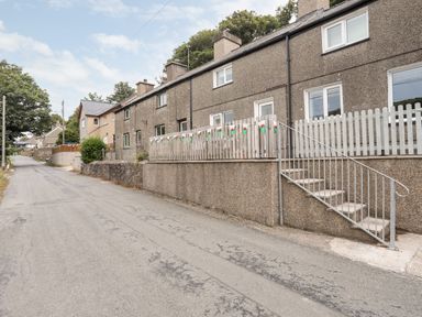 A row of connected houses with front steps and a small fenced area decorated with bunting on a quiet street at Isfryn in Llanengan near Abersoch