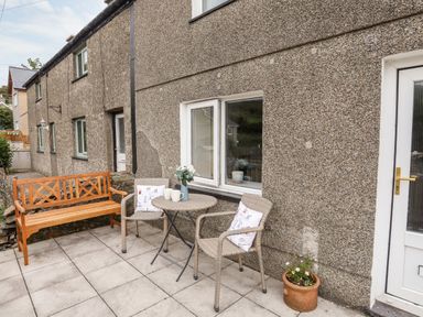 An outdoor patio with a wooden bench two wicker chairs a round table with mugs and a vase flowers and a potted plant at Isfryn Llanengan near Abersoch