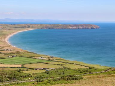 A coastal landscape with fields and a curved beach along a blue sea at Isfryn in Llanengan near Abersoch