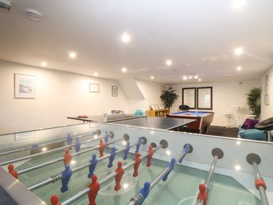 A game room with a foosball table, ping pong table, pool table, chairs, plants, and framed pictures on the walls at Coverack in Mawnan Smith Near Falmouth