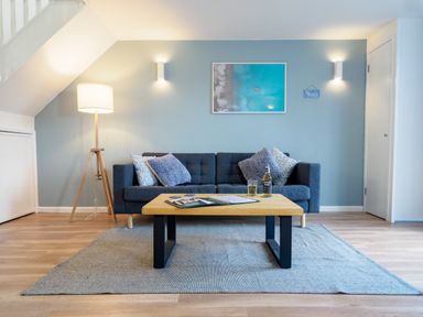 A living room with a dark blue sofa four pillows a wooden coffee table and a floor lamp at Coverack in Mawnan Smith Near Falmouth