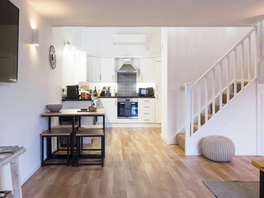 A kitchen with white cabinets a stove and a microwave next to a staircase with a knitted pouf at Coverack in Mawnan Smith Near Falmouth