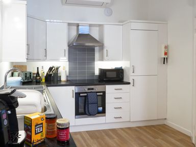 A kitchen with white cabinets and drawers a stainless steel oven and hood a black microwave on the counter a coffee machine and food jars on the counter at Coverack in Mawnan Smith Near Falmouth