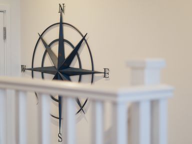 A wall-mounted metal compass rose decoration behind a white stair railing