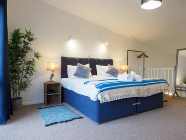 A bedroom with a double bed two bedside tables with lamps a plant a full length mirror and a clothes rack at Coverack in Mawnan Smith Near Falmouth