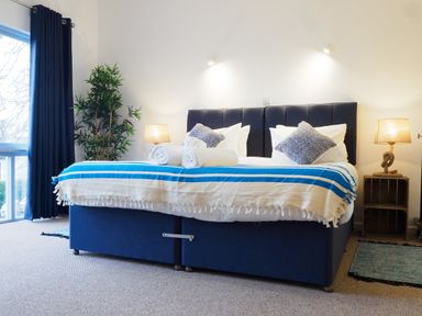A bedroom with a double bed with blue and white bedding two lamps and a plant at Coverack Mawnan Smith Near Falmouth