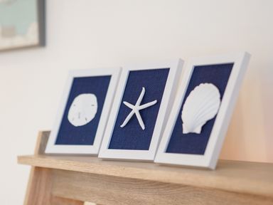 Three white-framed pictures with sea-themed decorations on a wooden shelf at Coverack in Mawnan Smith Near Falmouth