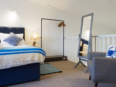 A bedroom with a bed a lamp a full-length mirror a clothing rack and an armchair at Coverack in Mawnan Smith Near Falmouth