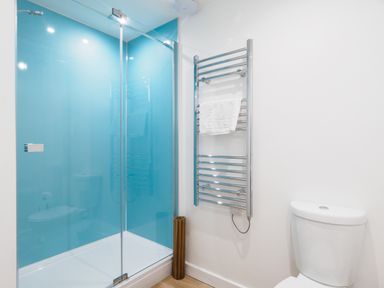 A bathroom with a glass shower enclosure with blue walls a chrome towel warmer with a white towel and a white toilet at Coverack in Mawnan Smith Near Falmouth