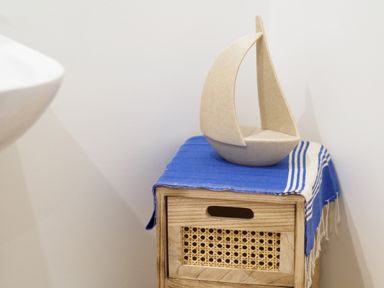 A small wooden cabinet with woven drawer and a blue striped cloth with a decorative sailboat on top at Coverack in Mawnan Smith Near Falmouth