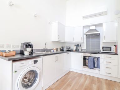 A kitchen with white cabinets a washing machine a coffee maker an oven a microwave and a sink at Helford in Mawnan Smith Near Falmouth