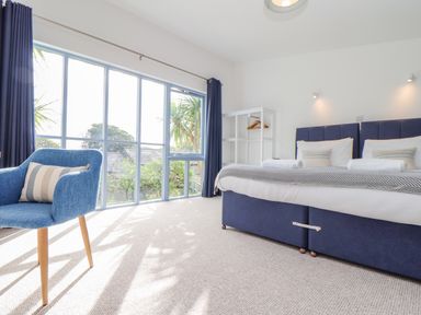 A bedroom with a blue upholstered bed blue chair and large windows at Helford in Mawnan Smith Near Falmouth