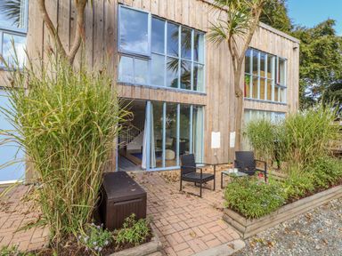 An outdoor patio area with two black chairs and a small table next to large windows and wooden building at Helford in Mawnan Smith Near Falmouth