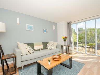 A living room with a grey sofa wooden coffee table and large sliding glass doors at Mousehole in Mawnan Smith Near Falmouth