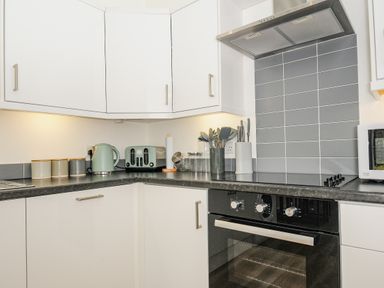 A kitchen corner with white cabinets black countertop and gray tiled backsplash in Mousehole Mawnan Smith Near Falmouth
