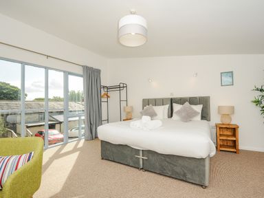 A bedroom with a bed two bedside tables a green chair a black clothes rack and large windows at Mousehole in Mawnan Smith Near Falmouth