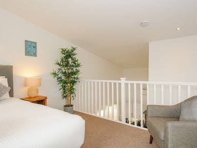 A bedroom with a bed a bedside table with a lamp a potted plant and an armchair at Mousehole in Mawnan Smith Near Falmouth