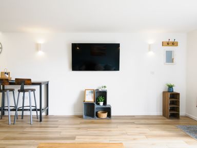 A living room with a wall mounted television wooden stools and tables wooden shelves with plants and decorations at Sennen in Mawnan Smith Near Falmouth