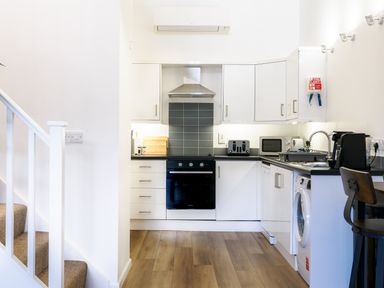 A kitchen with white cabinets black countertops a black oven a toaster microwave and washing machine at Sennen Mawnan Smith Near Falmouth