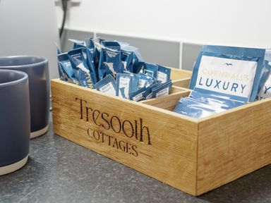 A wooden box with coffee and sugar packets next to two blue mugs at Tresooth Cottages