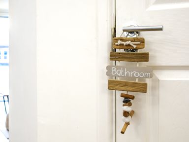 A white door with a modern silver handle and a wooden sign hanging that says Bathroom at Sennen in Mawnan Smith Near Falmouth
