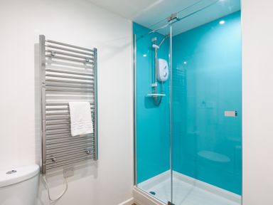 A bathroom with a glass shower enclosure with blue walls and a heated towel rail with a white towel at Sennen in Mawnan Smith Near Falmouth