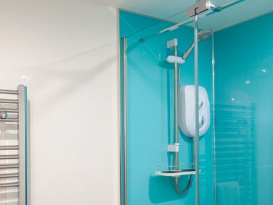 A shower area with a blue wall panel a showerhead and a towel rail at Sennen in Mawnan Smith Near Falmouth