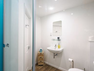 A bathroom with a wall-mounted sink mirror small cabinet and toilet paper holder at Sennen in Mawnan Smith Near Falmouth