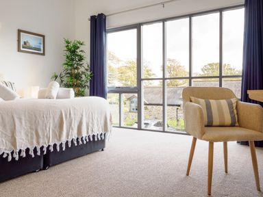 A bedroom with a bed near a large window and a chair with a striped pillow at Sennen in Mawnan Smith Near Falmouth