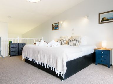 A bedroom with a bed with blankets and pillows a blue nightstand with a lamp and a black dresser at Sennen in Mawnan Smith Near Falmouth