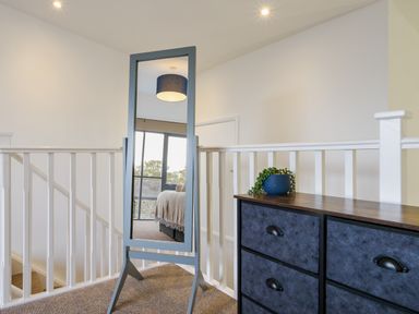 A hallway with a standing mirror reflecting a bedroom and a chest of drawers with a plant on top at Sennen in Mawnan Smith Near Falmouth