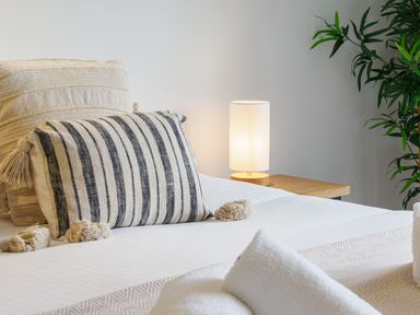 A bed with patterned cushions a bedside table with a lamp and a plant at Sennen in Mawnan Smith Near Falmouth
