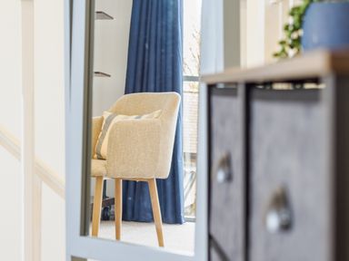 A beige armchair with a striped cushion in front of blue curtains near a window at Sennen in Mawnan Smith Near Falmouth