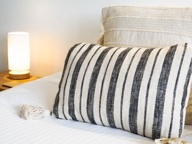 A bed with two decorative pillows and a lit table lamp on a wooden nightstand at Sennen in Mawnan Smith Near Falmouth