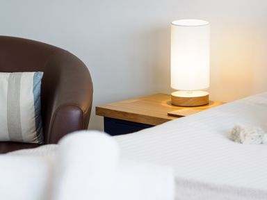 A brown leather chair with a striped cushion next to a wooden bedside table with a lamp and a white bed in the foreground at Sennen Mawnan Smith Near Falmouth