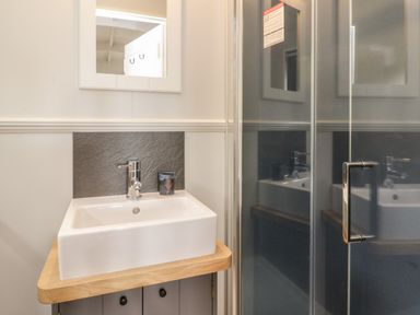 A bathroom sink with a faucet and soap dispenser next to a glass shower door at Coraldie Laggan near Newtonmore