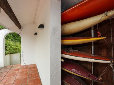 A tiled outdoor corridor with an archway and kayaks stacked on racks inside a storage area at Ynys Castell in Menai Bridge