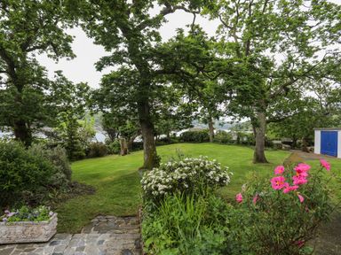 A garden with trees flowers and a shed near a body of water at Ynys Castell in Menai Bridge