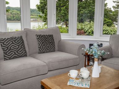 A living room with two gray sofas black patterned cushions a wooden coffee table with cups a teapot a vase with flowers and a magazine at Ynys Castell Menai Bridge