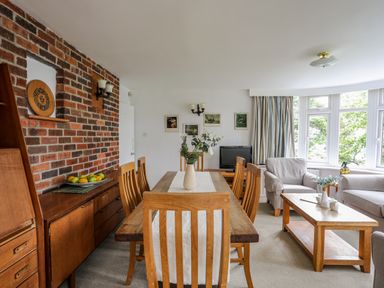 A dining area with a wooden table and chairs next to a brick wall and a living area with armchairs and a coffee table at Ynys Castell Menai Bridge