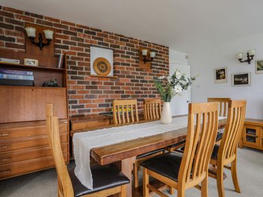 A dining room with wooden table and chairs a vase with flowers on the table and brick wall at Ynys Castell in Menai Bridge