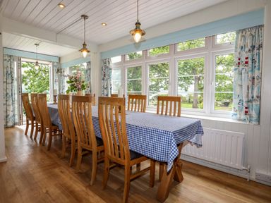 A dining room with a long wooden table covered with a blue checkered tablecloth and wooden chairs at Ynys Castell in Menai Bridge