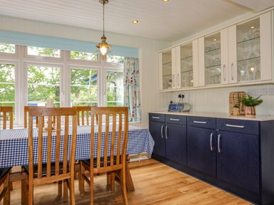 A dining room with wooden chairs and blue checkered tablecloth next to blue and white cabinets at Ynys Castell in Menai Bridge